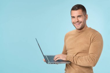 Happy young man using laptop and looking at camera over blue background