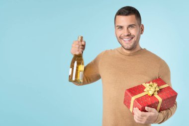 Happy young man holding present and champagne bottle isolated on blue background. Celebration concept