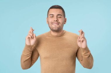 Young handsome man over isolated blue background with fingers crossing making a wish