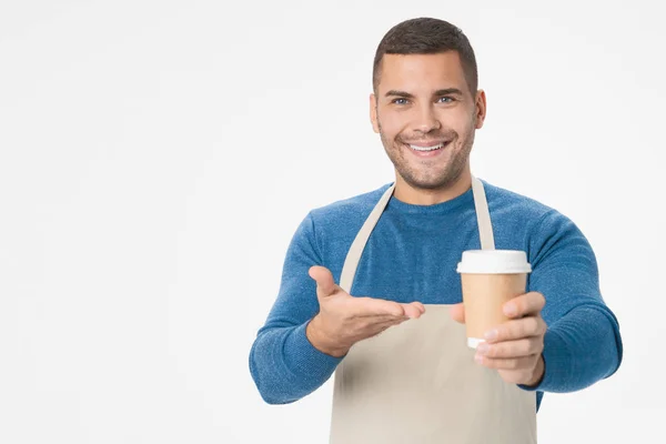 Positive handsome man holding paper cup recommending you to taste it wearkng apron isolated over white background — Stock Photo, Image