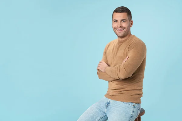 Portrait of handsome young man in casuals sitting on the chair over blue background — 스톡 사진