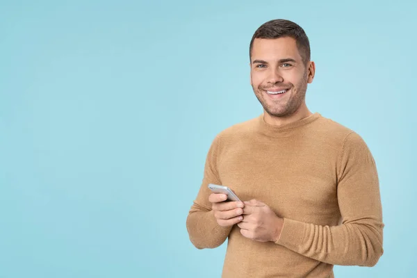 Lächelnder junger Mann mit Handy isoliert vor blauem Hintergrund — Stockfoto