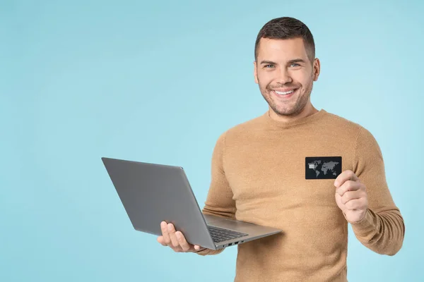 Flot mand iført afslappet tøj ved hjælp af bærbar computer og viser kreditkort stående isoleret over blå baggrund - Stock-foto