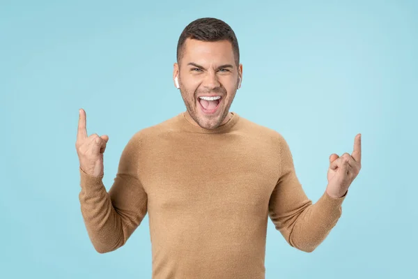 Young man showing rock sign while listening music isolated on blue background — 스톡 사진