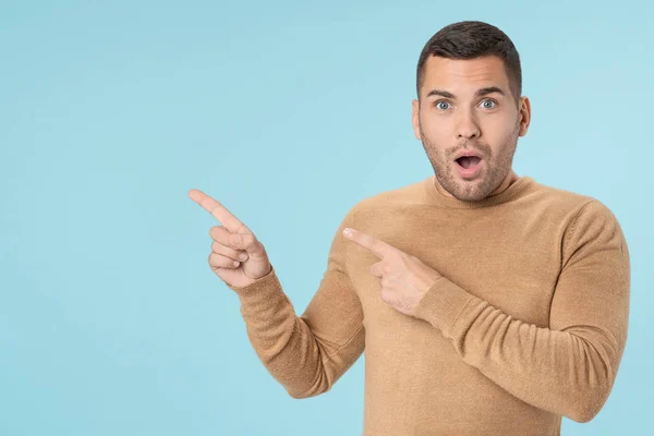 Uomo sorpreso puntando il dito verso lo spazio di copia isolato su sfondo blu — Foto Stock