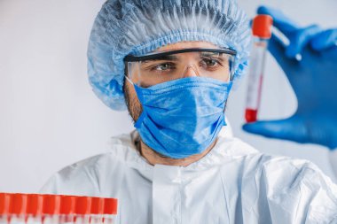 Yüz maskeli doktor virüs enfeksiyonlu kan örnekleri için vakum tüpleri kontrol ediyor.