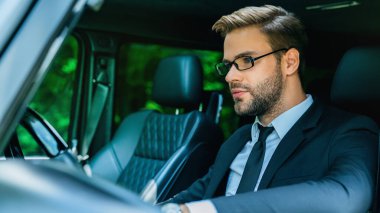 Resmi takım elbiseli yakışıklı genç adam araba kullanırken düzgün görünüyor.