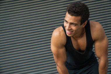 Gülümseyen genç adam, koşudan sonra dinleniyor, gri arka planda, şehir caddesinde dururken.