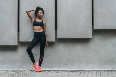 Sporda tam boy formda genç bir kadın dışarıda dikilip duruyor.