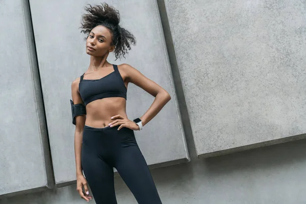 Tough young african woman in sports wear and curly hair taking break after running staring at camera