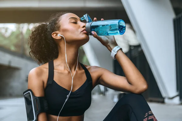 African fitness woman drinking water from bottle after workout outdoors