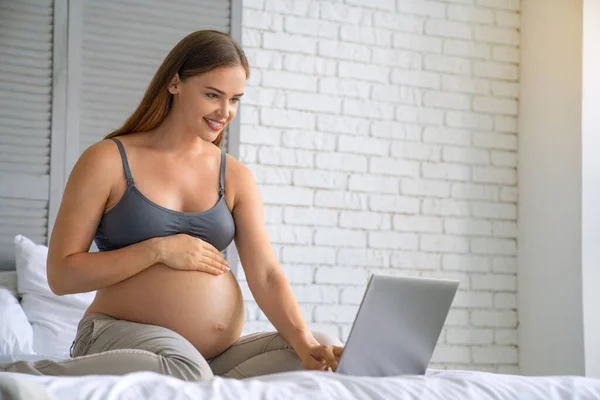 若いです妊娠中の女性リラックス上のソファとともにラップトップ上のホームインテリア背景 — ストック写真