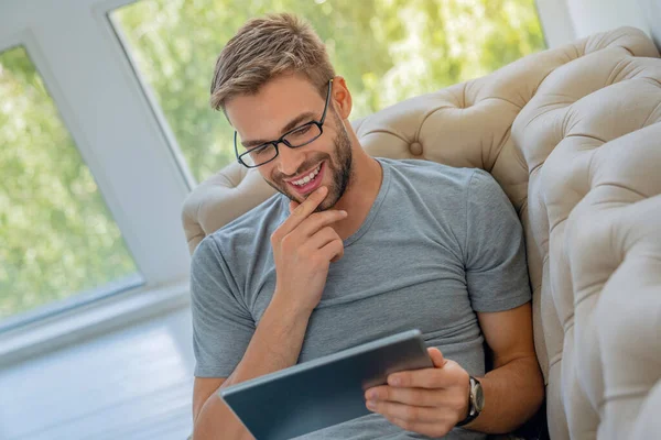 Bonito Homem Está Usando Tablet Digital Sorrindo Enquanto Descansa Sofá — Fotografia de Stock