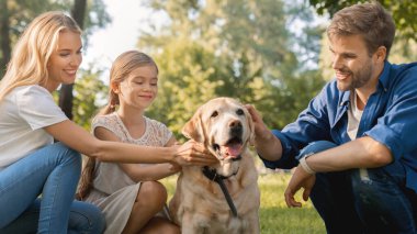 Mutlu ebeveynlerin küçük kızlarıyla dışarıda köpekle eğlenirken yakın plan çekimleri.