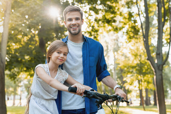Cute smiling girl learning to ride a bicycle with her father out