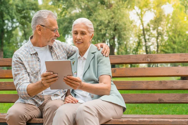 ハッピー退職したカップルは公園のベンチに座って デジタルタブレットを使用して — ストック写真