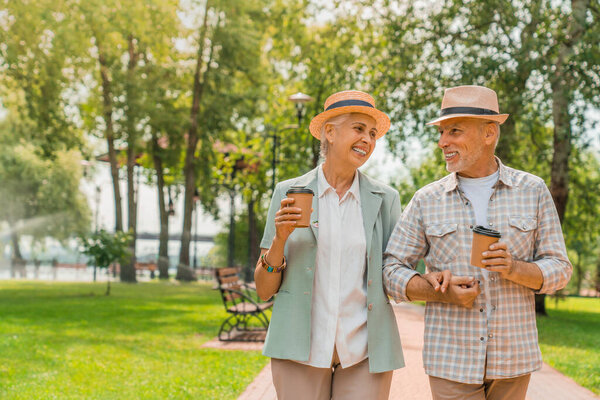 Счастливые пожилые мужчина и женщина, гуляющие в парке и пьющие кофе
