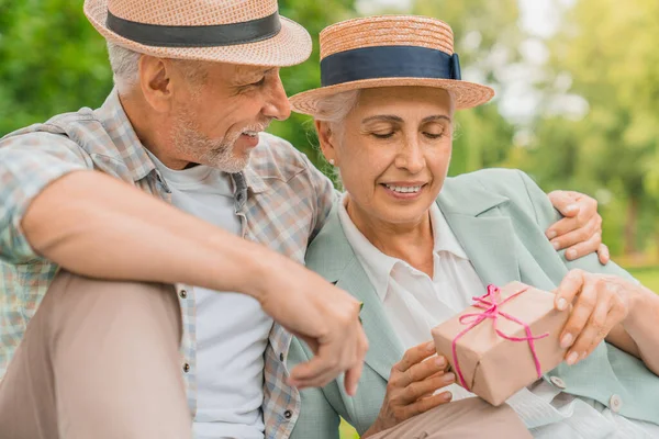 Vidám Öregember Néz Feleségére Miközben Egy Szép Ajándékdobozt Neki Születésnapjára — Stock Fotó