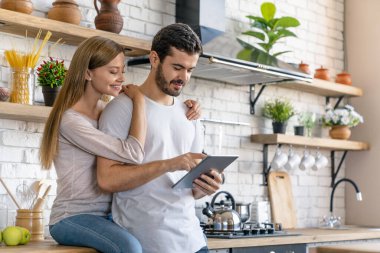 Güzel genç çift dijital tablet kullanıyor ve evde yemek pişirirken gülümsüyor.