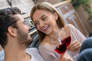 Mutlu çiftin mutfak zemininde oturmuş şarap kadehleriyle birbirlerine baktıkları yakın çekim.