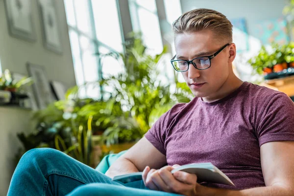 Attractive young man with glasses focused reading book while taking break at coworking space