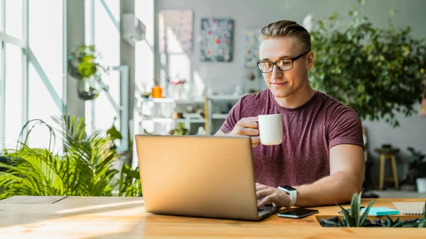 Imagem Frontal Jovem Empresário Sorrindo Bebendo Café Enquanto Usa Laptop — Fotografia de Stock