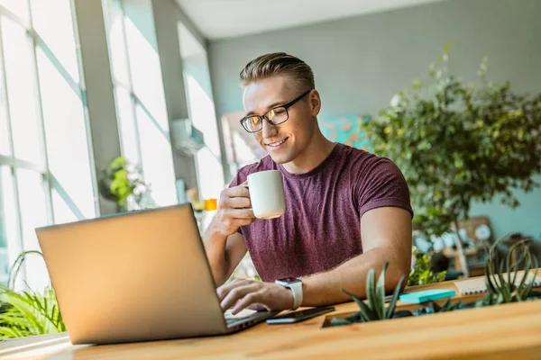 Jovem Empresário Alegre Bebendo Café Enquanto Usa Laptop Escritório — Fotografia de Stock