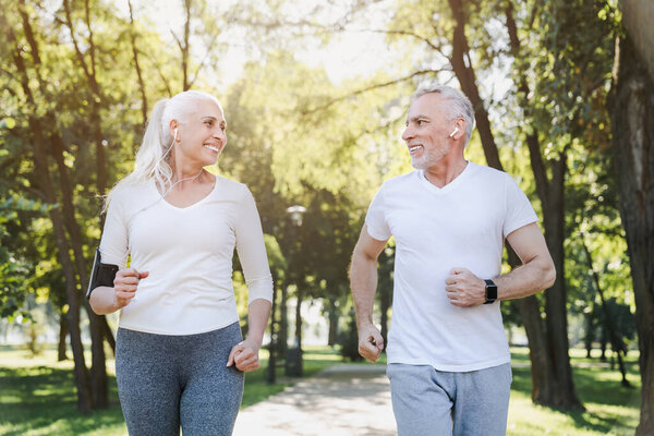 Elderly man and old woman in headphones jogging together outside