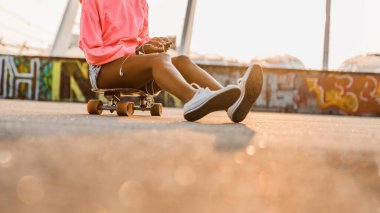 Kaykayının üstünde kulaklıklarla oturan kızın kırpılmış görüntüsü.