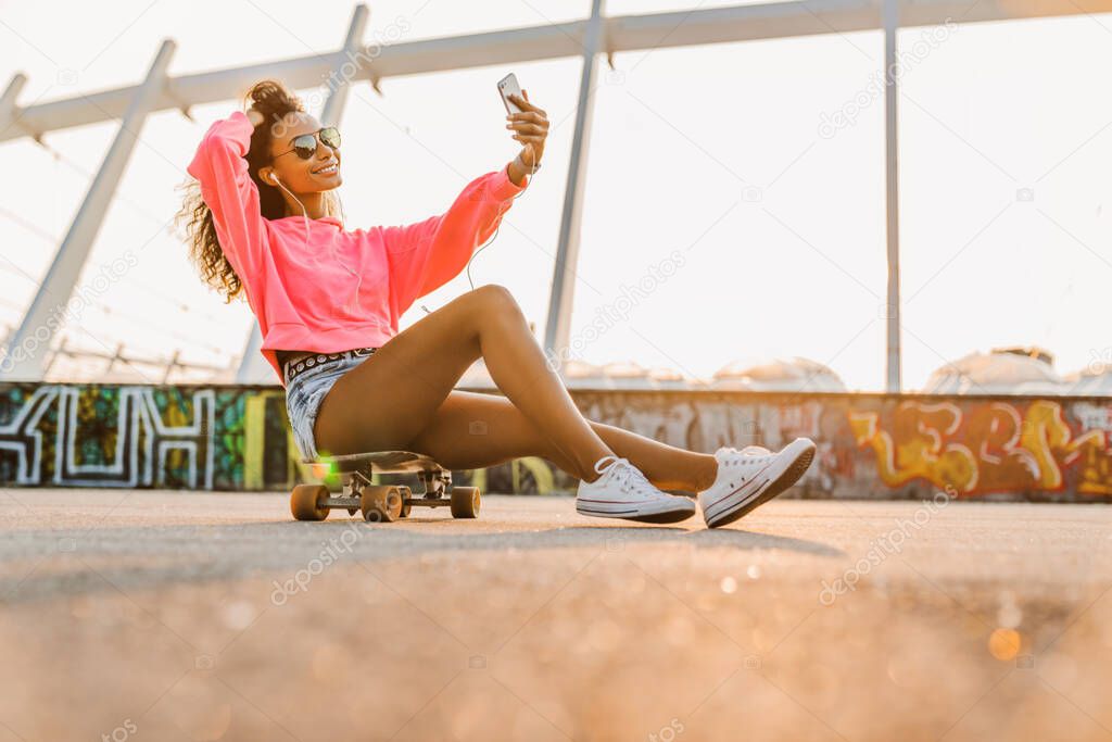 Young african skater girl taking selfie with her phone while being at city