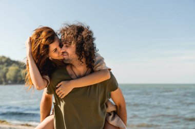 Romantik genç çift yaz tatilinin tadını çıkarıyor. Güneşli sahilde öpüşen bir kadın.