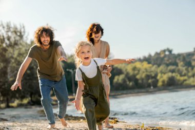 Genç ve mutlu bir aile sahilde eğleniyor. Kumsalda koşan küçük tatlı bir kız ailesi tarafından kovalanır..