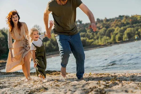 가족들 해변에서 즐거운 시간을 보내고 해변을 뛰어가는 귀여운 소녀가 부모에게 — 스톡 사진