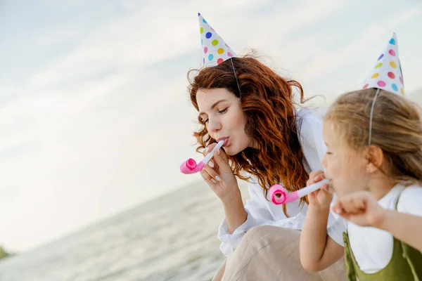 Mother Little Girl Wearing Party Hats Sitting Beach Blowing Whistles — Stock Photo, Image