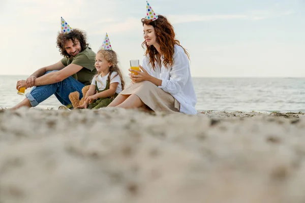Low angle view of family with party hats drinking orange juice on the beach