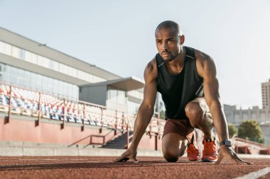 Spor pistinde koşmak için başlangıç pozisyonunda olan genç bir sporcunun düşük açılı görüntüsü