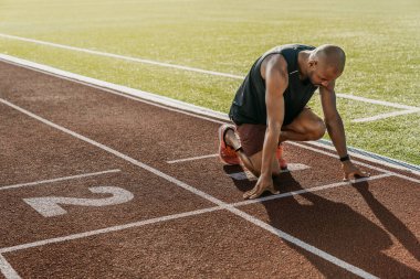 Spor pistinde koşmak için başlangıç pozisyonunda genç bir sporcu.
