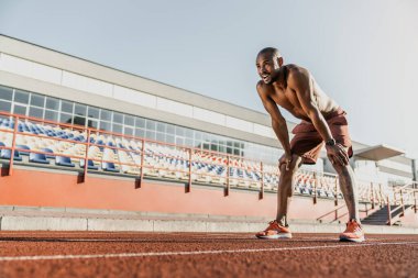 Erkek koşucu ellerini dizlerinin üstüne koyup koşu yolunda dinleniyor.