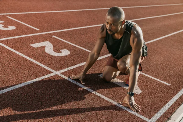 Young male athlete at starting block on running track preparing for run