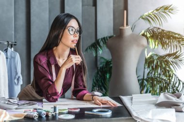 Stüdyoda dururken eskizler üzerinde çalışan güzel Asyalı kadın.