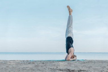 Genç sağlıklı bir adam plajda yoga egzersizleri yapıyor, dengede duruyor.