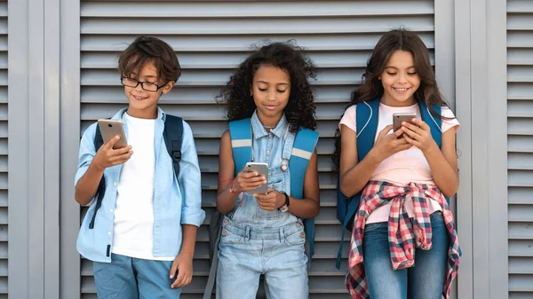 Gülümseyen Okul Çocukları Sokakta Gri Arka Planda Duran Akıllı Telefonları — Stok fotoğraf