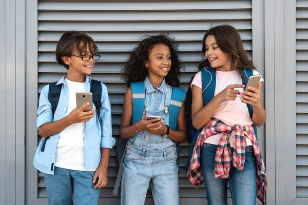 Улыбающиеся Школьники Пользующиеся Смартфонами Смотрящие Мобильный Телефон Улице Стоящей Сером — стоковое фото