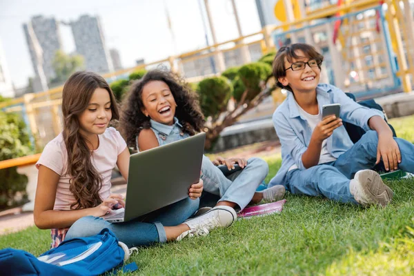 遊び場の芝生の上に座っている多民族小学校の子供たちのグループは ラップトップコンピュータを見て — ストック写真
