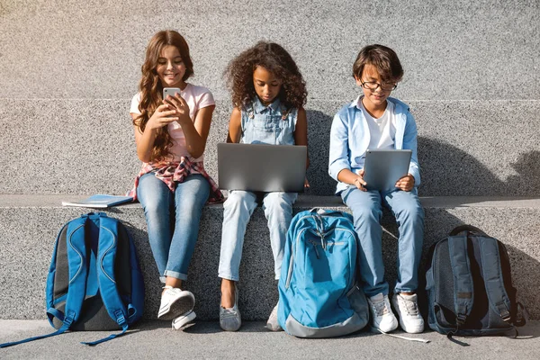 Gülümseyen Okul Çocukları Dijital Aletlerle Sokakta Oturuyorlar — Stok fotoğraf