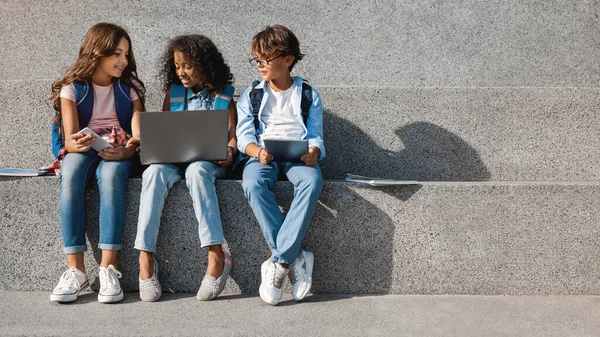 Crianças Escola Sorridentes Sentadas Olhando Smartphone Com Dispositivos Digitais Mãos — Fotografia de Stock