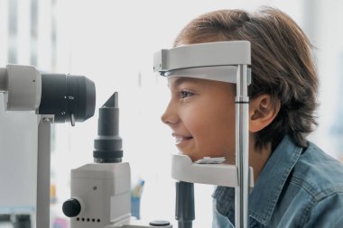 Göz kliniğinde tonometreyle görüşü kontrol eden çocuğun yan görüntüsü