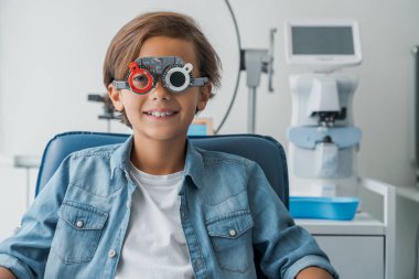 Tıbbi klinikte gözlük testine tabi tutulan gülümseyen bir çocuğun portresi.