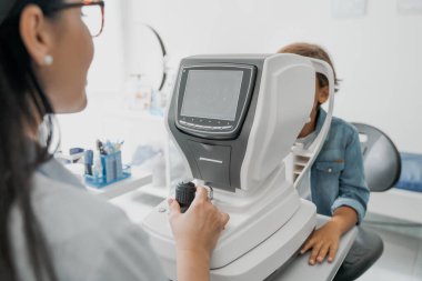 Kadın doktor, küçük çocuğu özel optik aparatlarla gözleri için test ediyor.