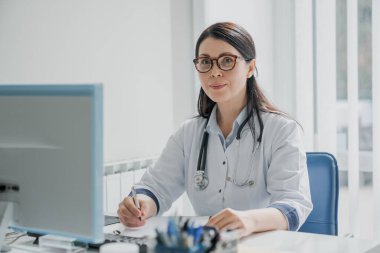 Masada oturan ve hastane ofisinde çalışan kadın doktor.